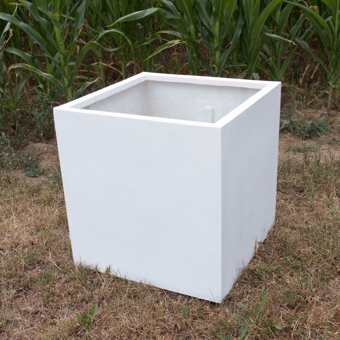 Leerer quadratischer Pflanzkübel aus Fiberglas in Perlmuttweiß auf trockener Wiese vor einem Maisfeld