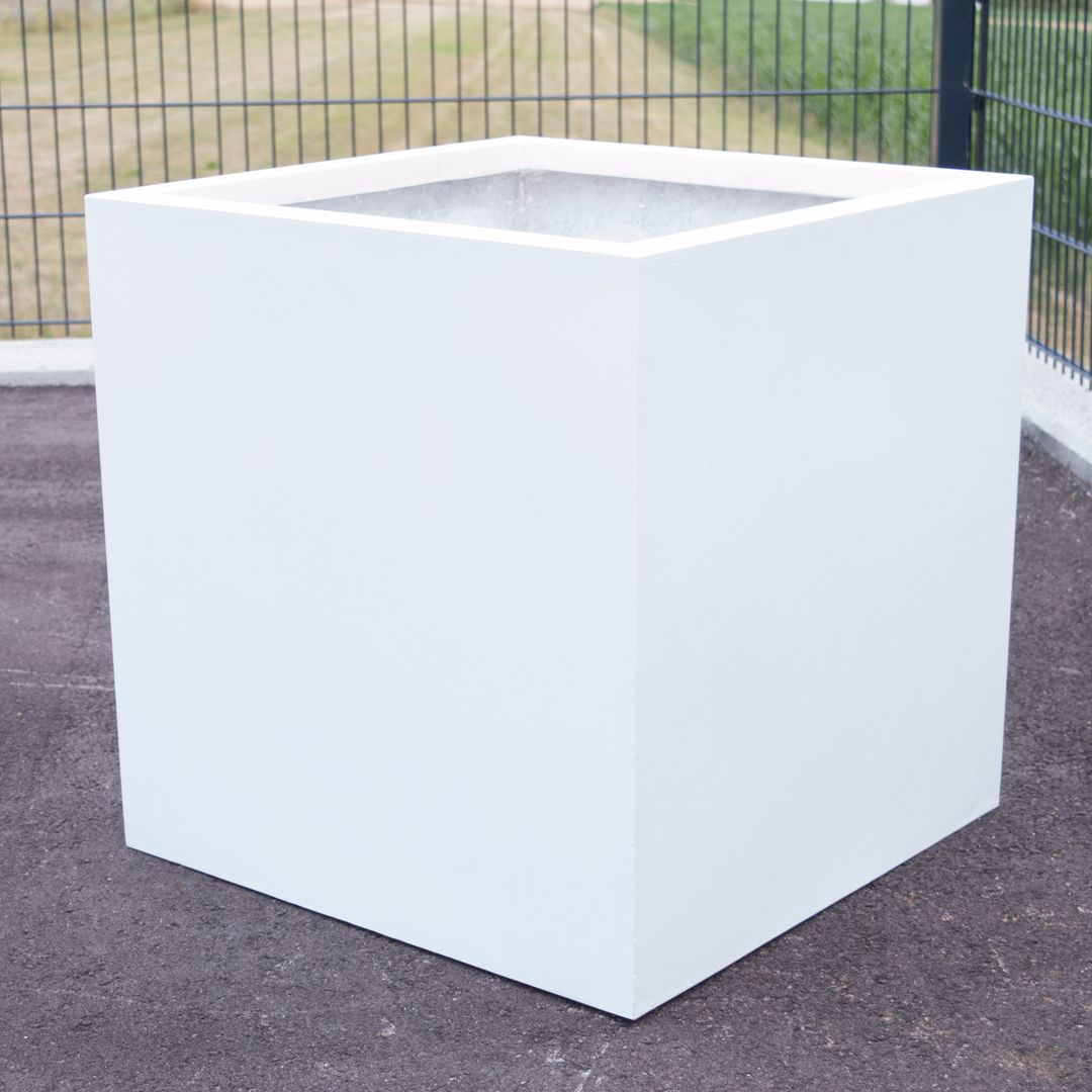 Quadratischer Pflanzkübel aus Fiberglas in Perlmuttweiß, leer auf einer Asphaltfläche vor einem Metallzaun im Freien