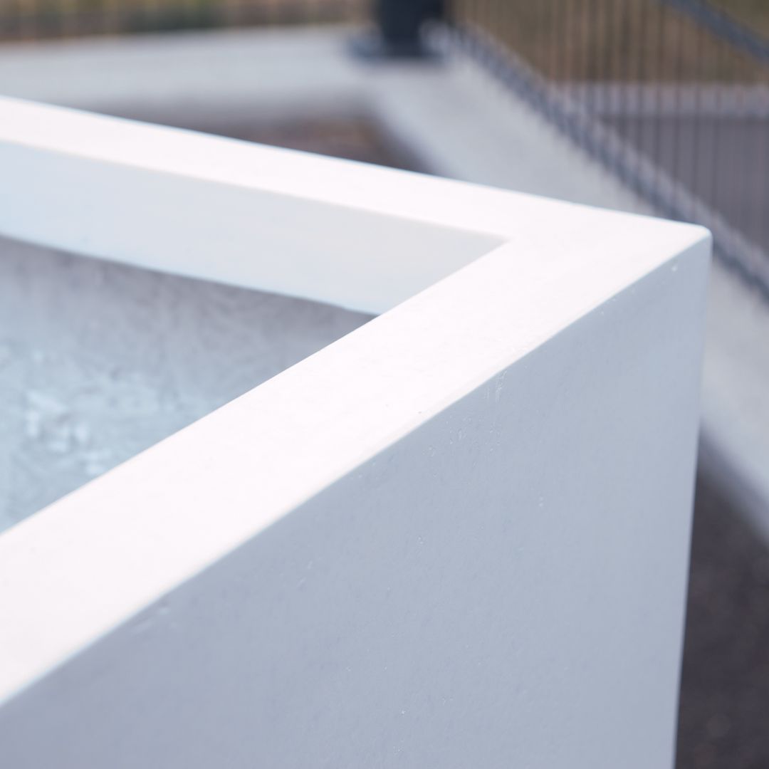 Nahaufnahme der Ecke eines quadratischen Pflanzkübels aus Fiberglas in Perlmuttweiß mit glatter, matter Oberkante