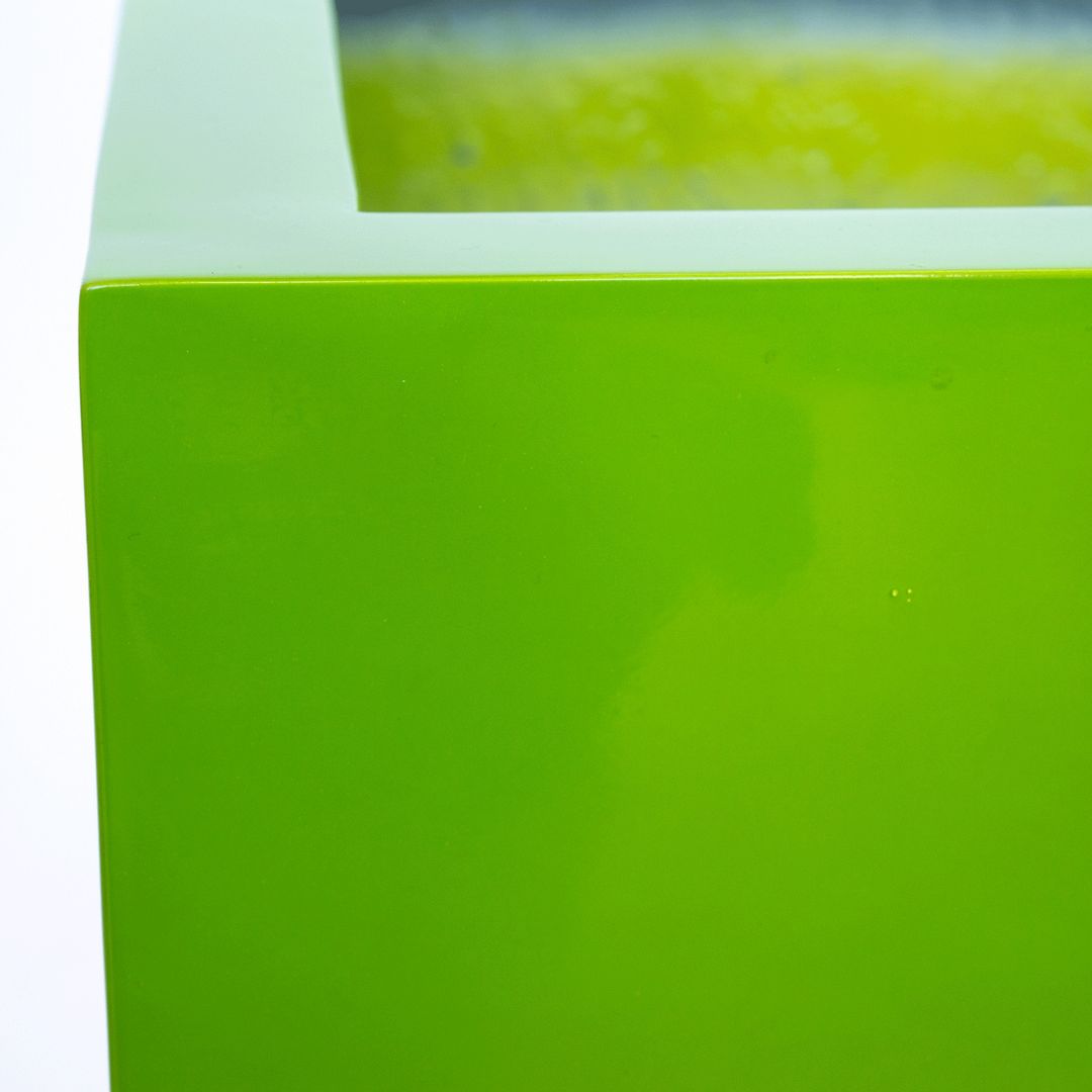 Nahaufnahme der Ecke eines quadratischen Pflanzkübels in Hochglanz Avocadogrün mit glänzender Oberfläche und Rand
