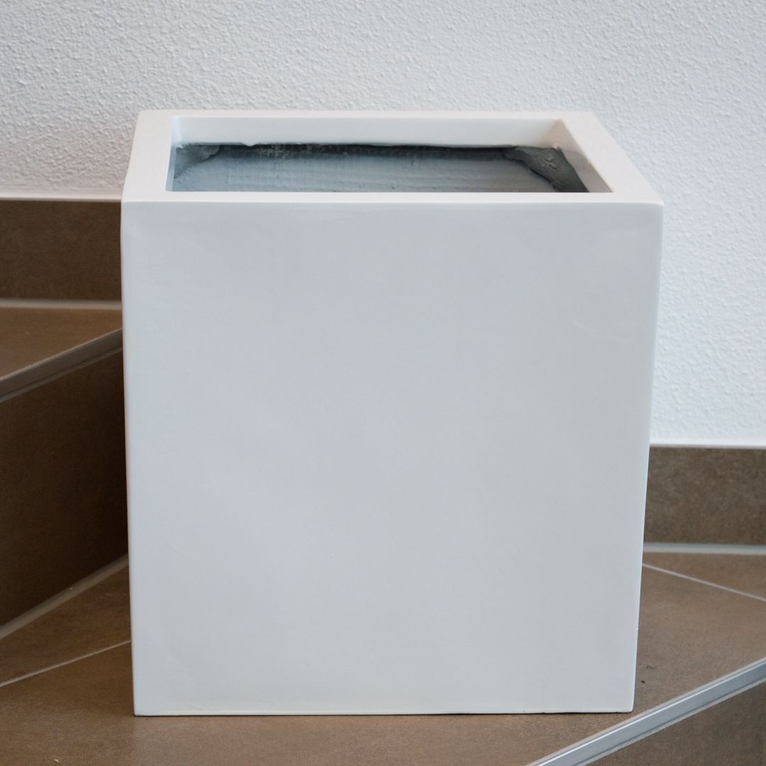 Quadratischer Pflanzkübel aus Fiberglas in Weiß ohne Bepflanzung auf einer gefliesten Treppenstufe vor heller Wand