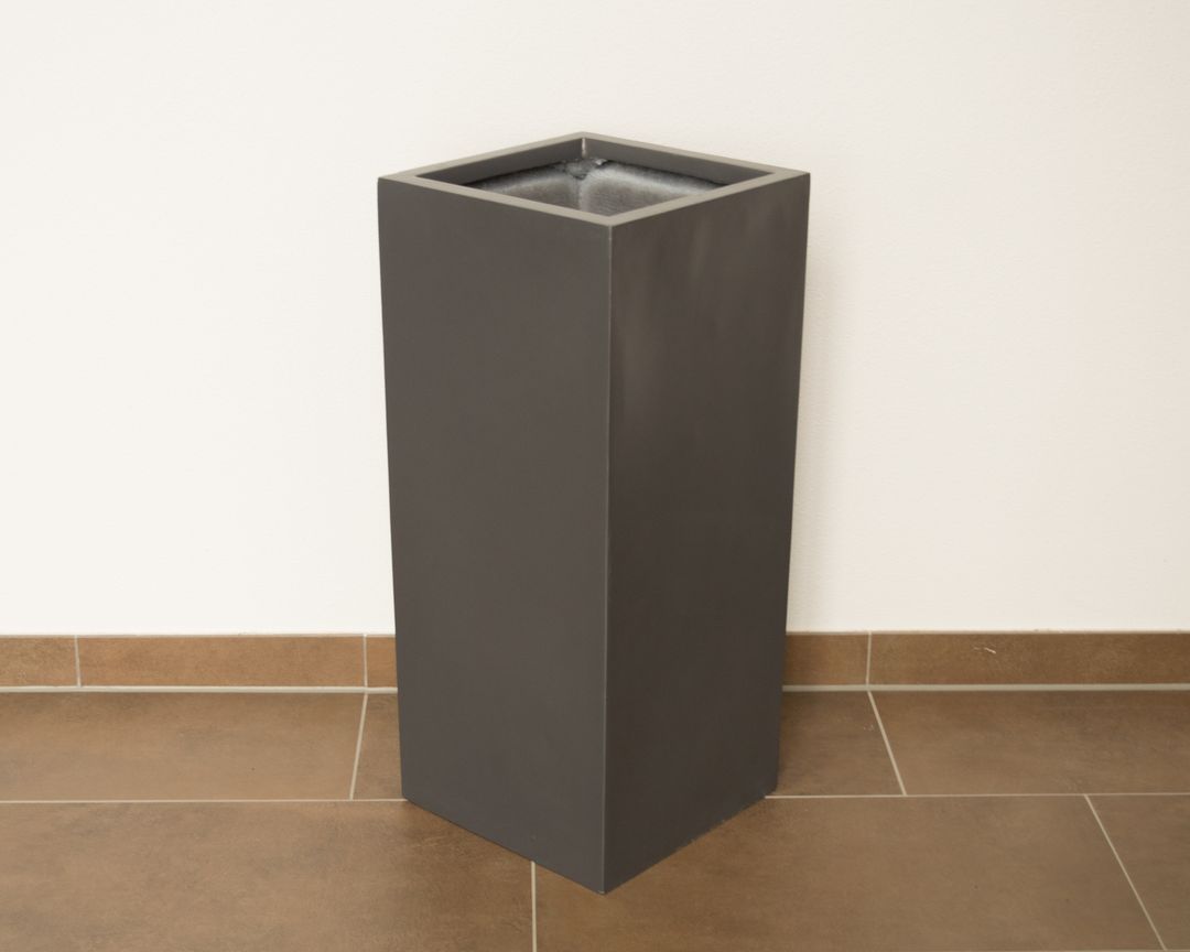 Hoher quadratischer Pflanzkübel in Säulenform in Anthrazit metallic, leer auf braunem Fliesenboden vor weißer Wand