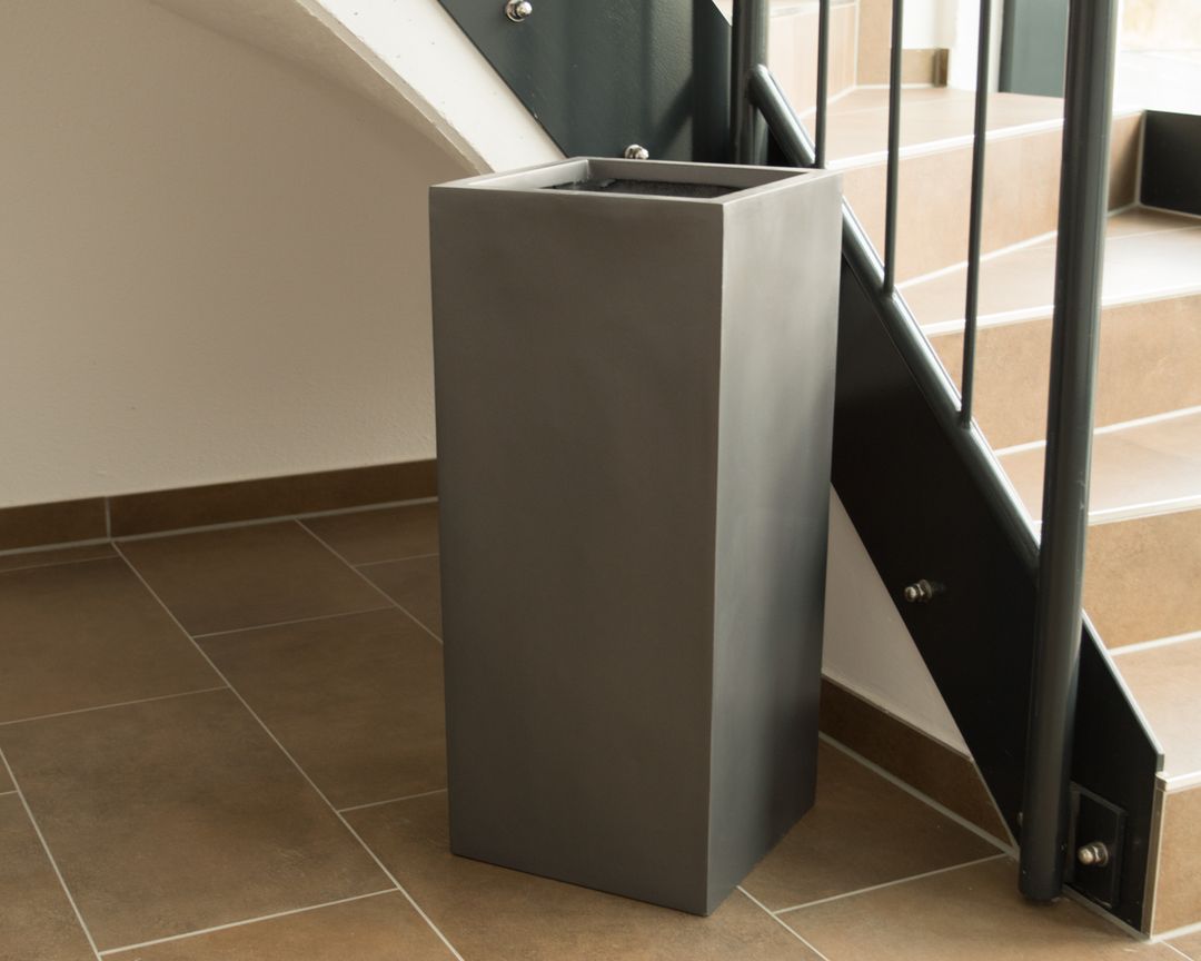 Pflanzkübel aus Fiberglas in Säulenform in Anthrazit metallic ohne Pflanze im Treppenhaus auf braunem Fliesenboden