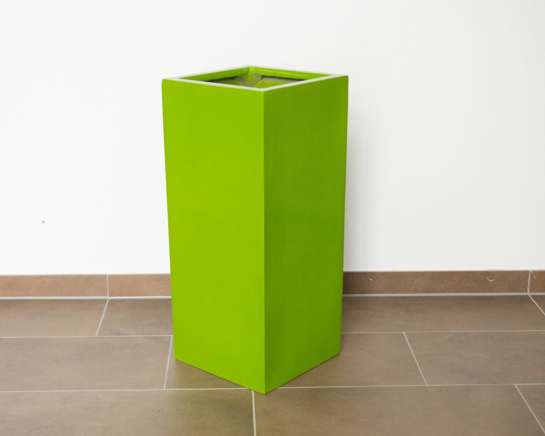 Quadratische Pflanzsäule aus Fiberglas in Hochglanz Avocadogrün, leer auf braunen Fliesen vor weißer Wand
