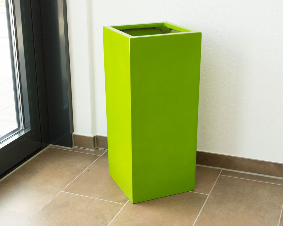 Hochglänzende Pflanzsäule aus Fiberglas in Avocadogrün, leer in einer Raumecke neben einer Glastür auf Fliesenboden