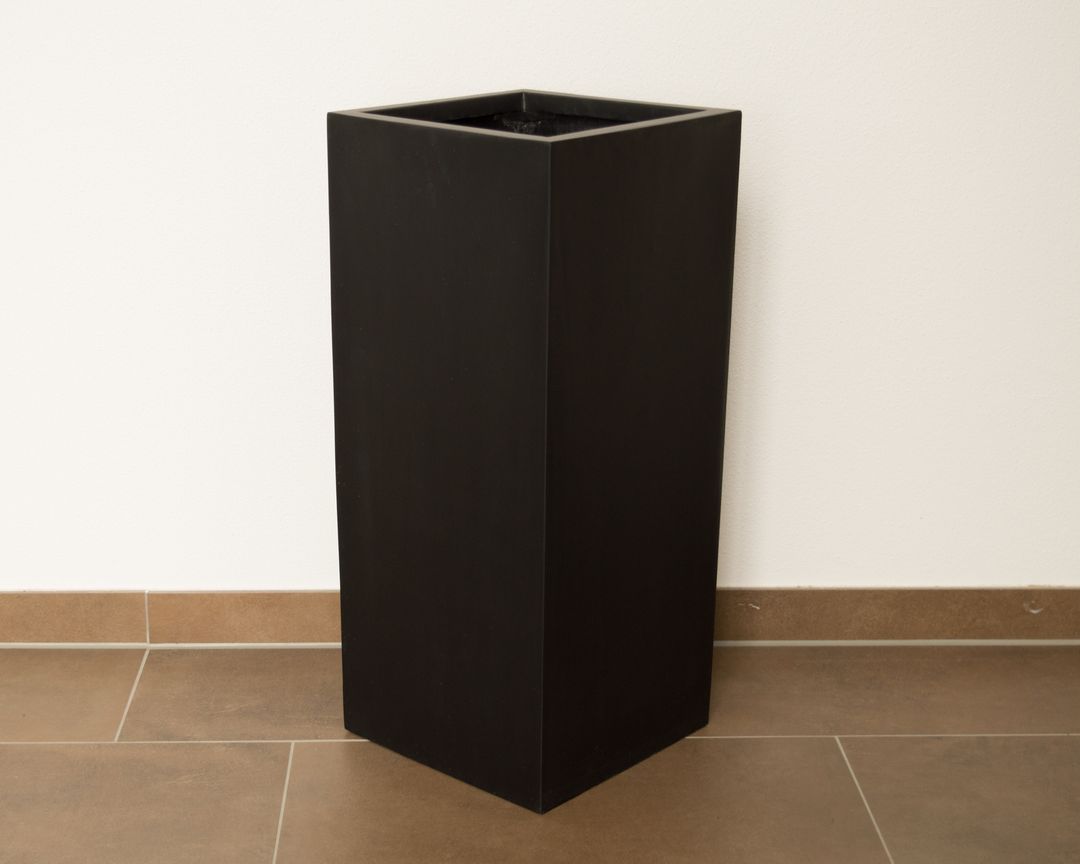 Schwarz-matter Pflanzkübel aus Fiberglas in hoher Säulenform, leer auf Fliesenboden vor heller Wand