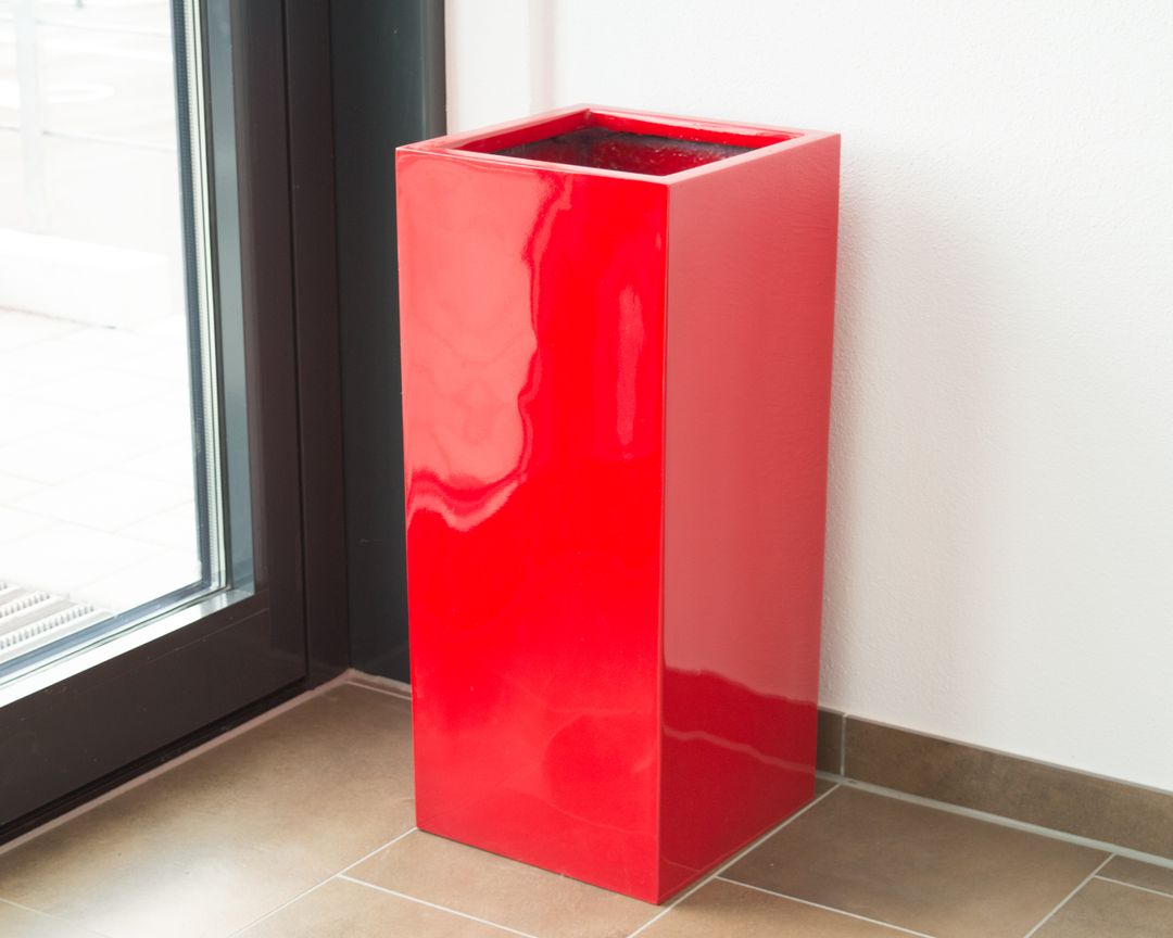 Hochglanz roter Pflanzkübel aus Fiberglas in Säulenform, leer, auf Fliesenboden neben einer Glastür