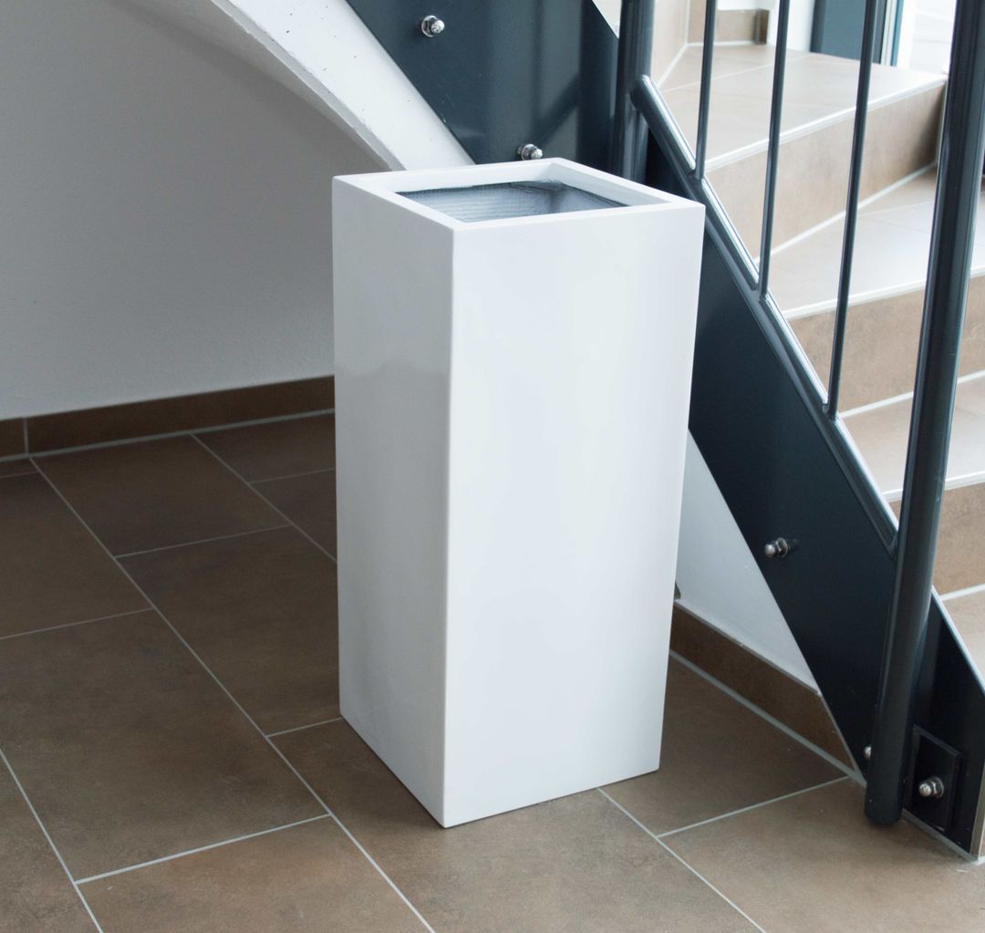 Hochglanz weißer Pflanzkübel aus Fiberglas in Säulenform, leer, neben einer Treppe auf braunem Fliesenboden