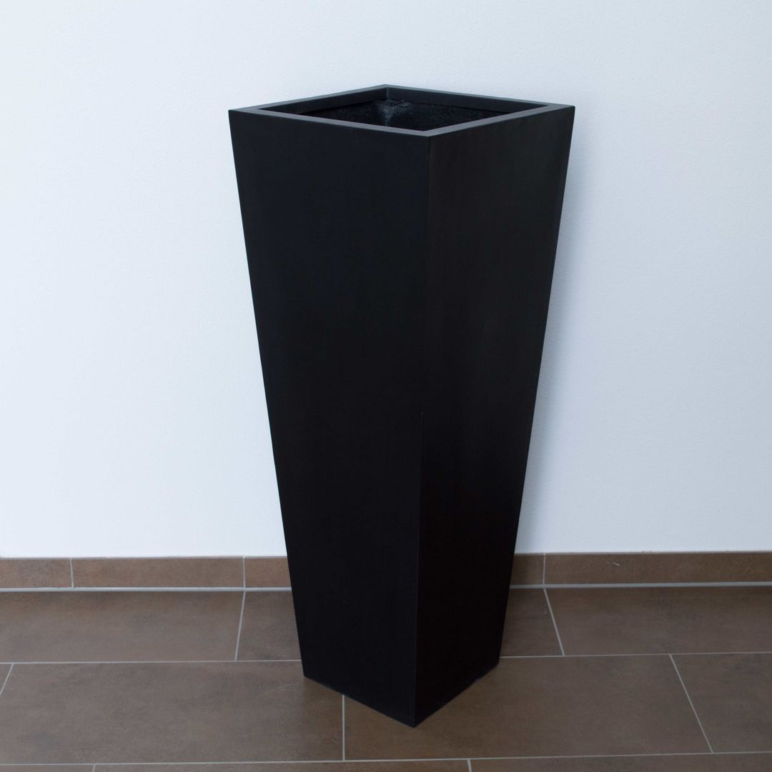 Hoher konischer Pflanzkübel aus Fiberglas in Schwarz-matt als quadratische Säule auf braunem Fliesenboden vor weißer Wand
