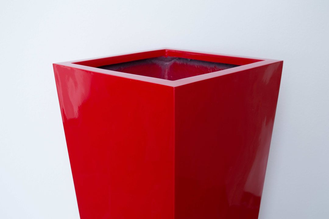 Oberer Teil einer konischen Pflanzsäule aus Fiberglas in Hochglanz Rot mit quadratischer Öffnung vor heller Wand