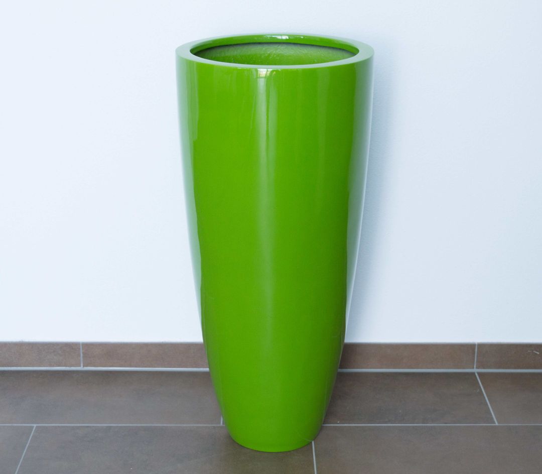 Runder konischer Pflanzkübel aus Fiberglas in Hochglanz Avocadogrün vor weißer Wand auf braunem Fliesenboden