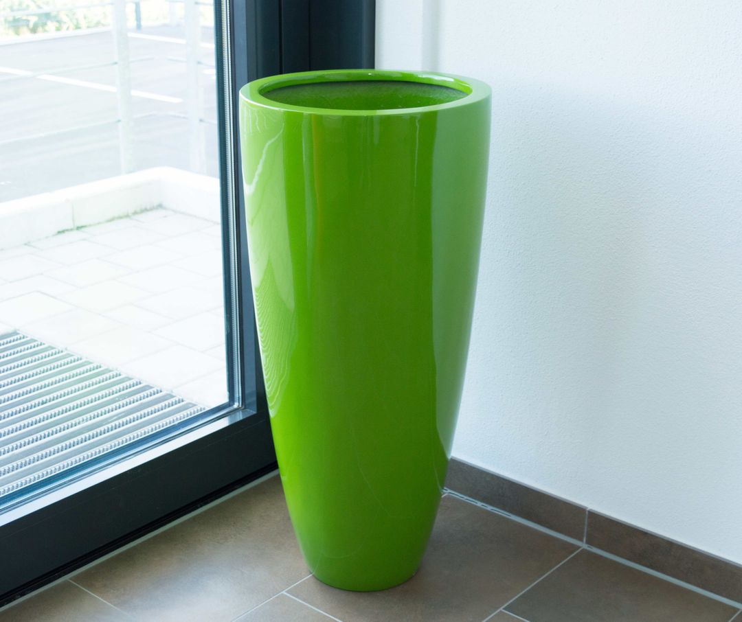 Hochglanz avocado grüner runder konischer Pflanzkübel aus Fiberglas ohne Bepflanzung in einer Zimmerecke neben einer Glastür