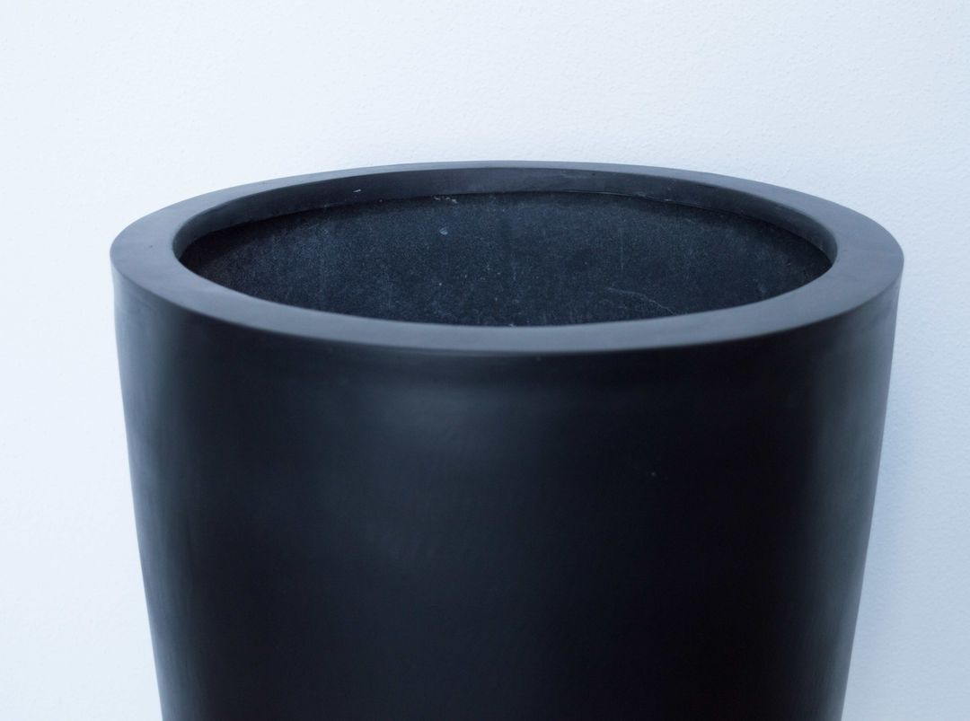 Oberer Rand und Innenraum eines runden konischen Pflanzkübels aus Fiberglas in Schwarz-matt vor heller Wand
