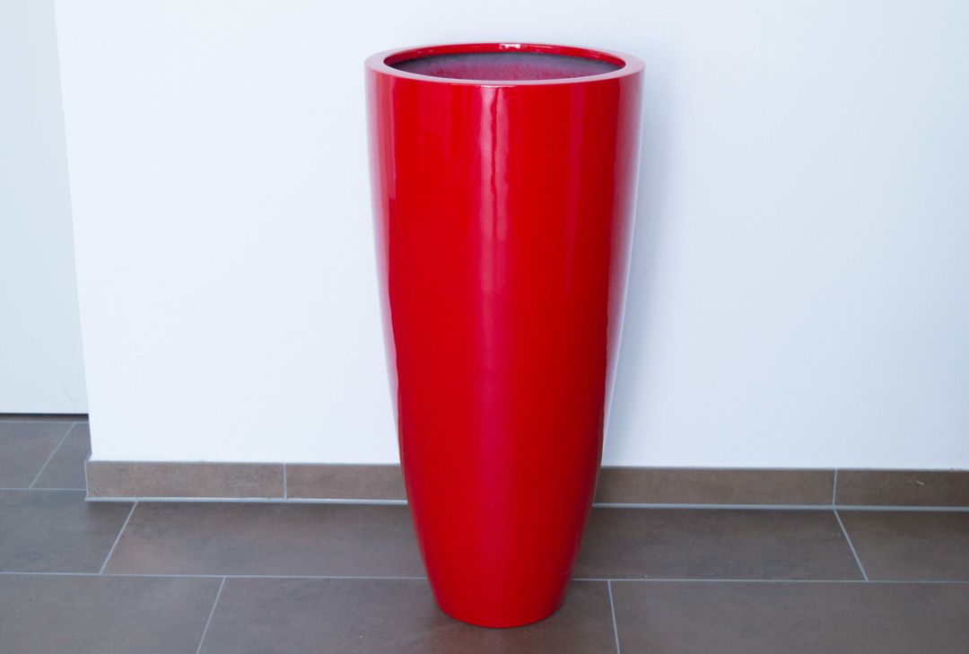 Hoher runder konischer Pflanzkübel aus Fiberglas in Hochglanz Rot, leer auf Fliesenboden vor weißer Wand