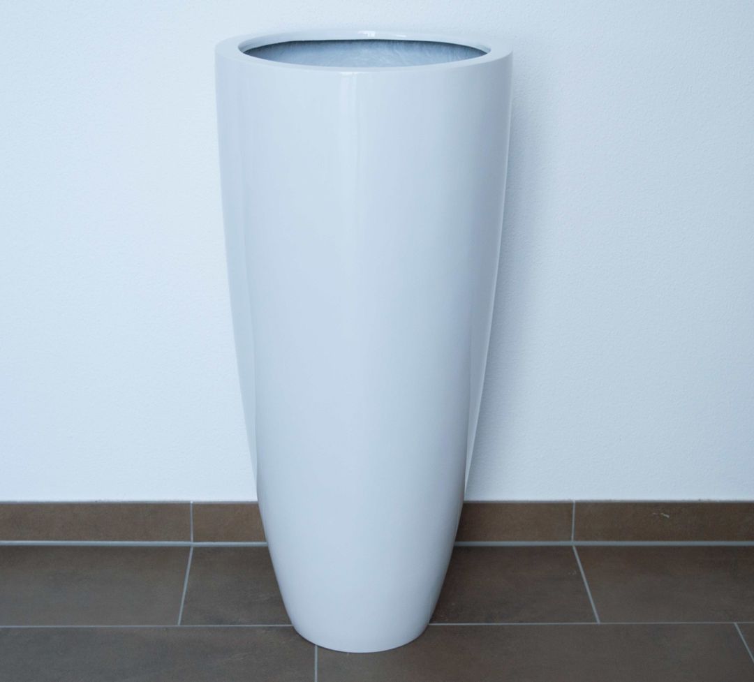 Hochglanz weißer runder konischer Pflanzkübel aus Fiberglas, leer, vor weißer Wand auf braunen Bodenfliesen