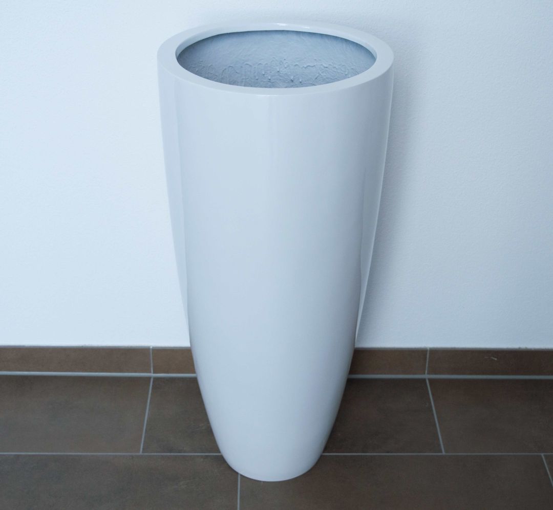 Hochglanz weißer, runder konischer Pflanzkübel aus Fiberglas, leer, vor weißer Wand auf braunem Fliesenboden