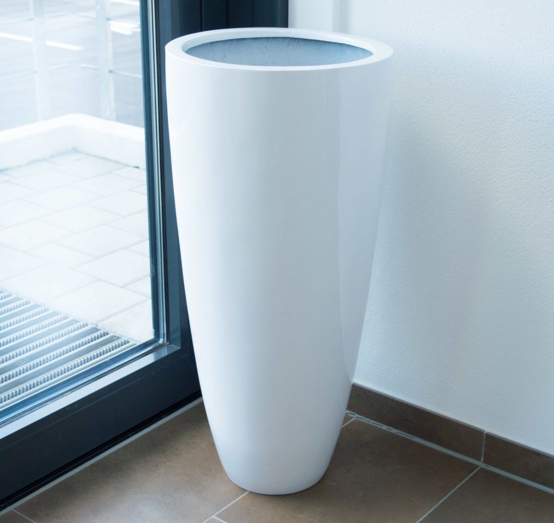 Hochglanz weißer runder konischer Pflanzkübel aus Fiberglas ohne Bepflanzung in einer Zimmerecke neben einer Glastür