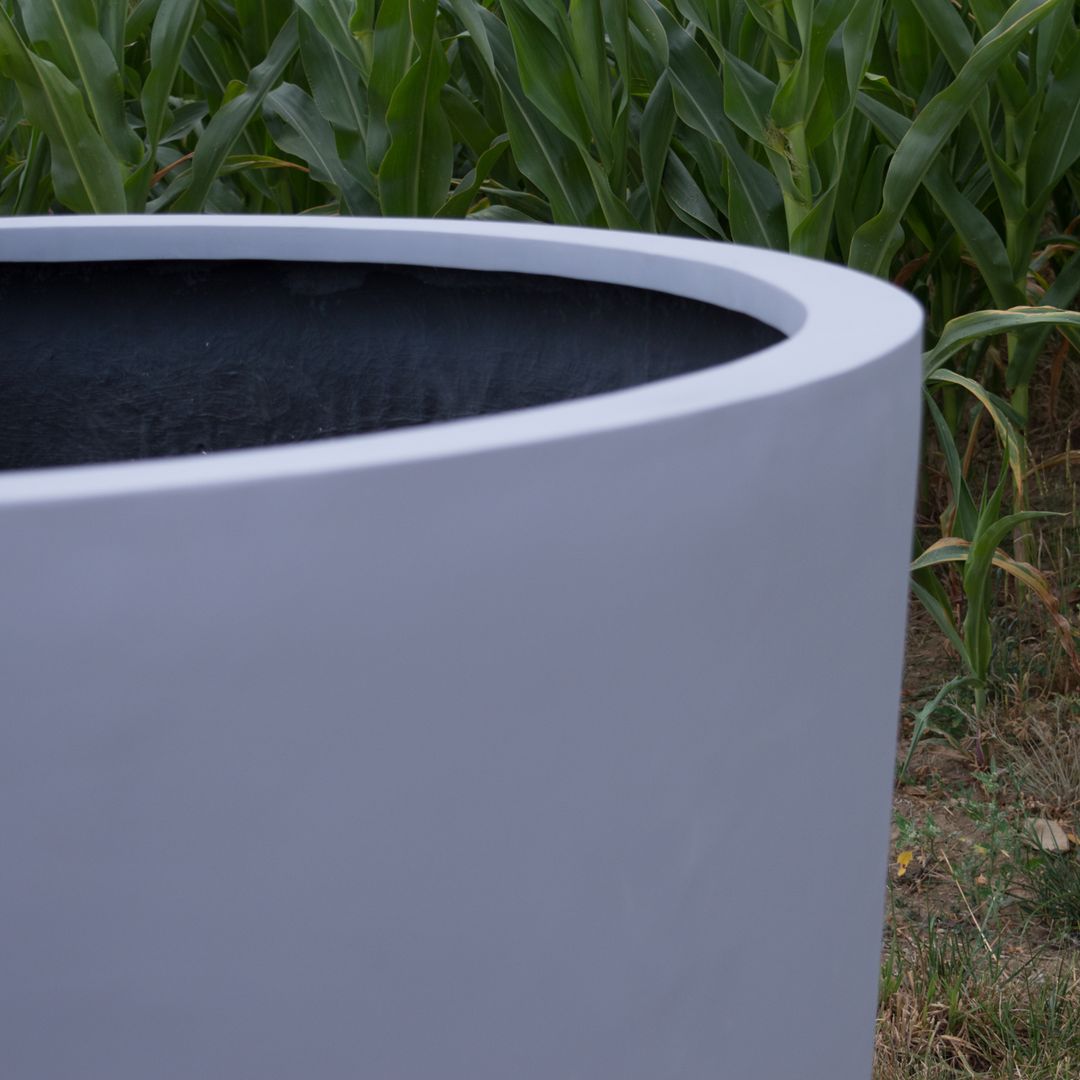 Ausschnitt eines grauen runden Pflanzkübels aus Fiberglas mit dunkler Innenseite vor einem Maisfeld