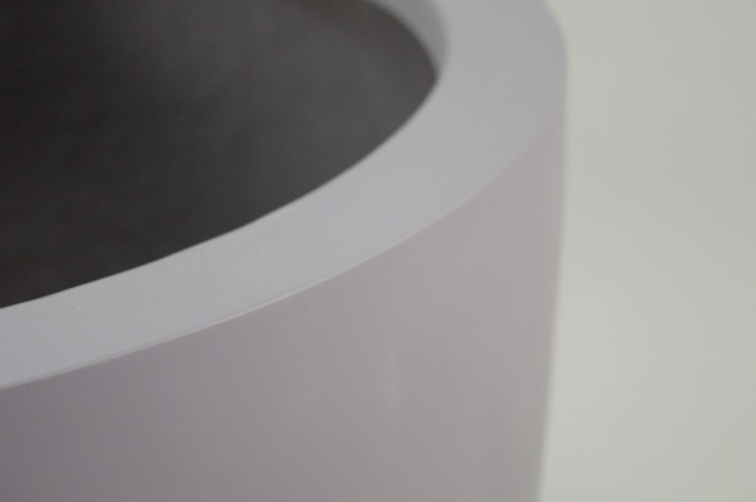 Nahaufnahme vom abgerundeten oberen Rand eines runden grauen Pflanzkübels aus Fiberglas mit matter Oberfläche
