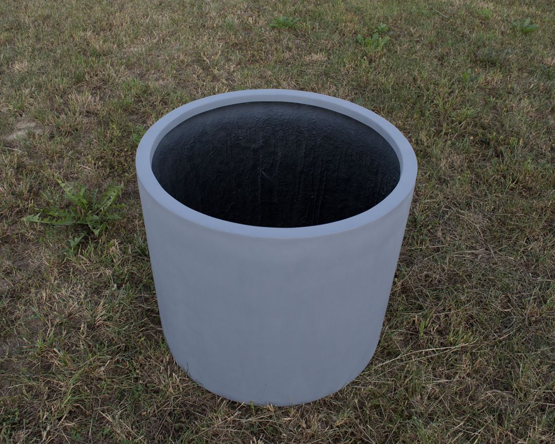 Leerer grauer zylindrischer Pflanzkübel aus Fiberglas auf einer Rasenfläche, Blick schräg von oben ins dunkle Innere