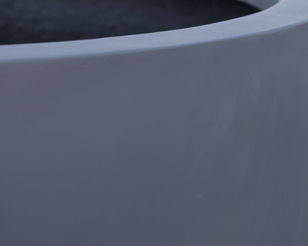Nahaufnahme von Rand und matter Außenwand eines grauen zylindrischen Pflanzkübels aus Fiberglas