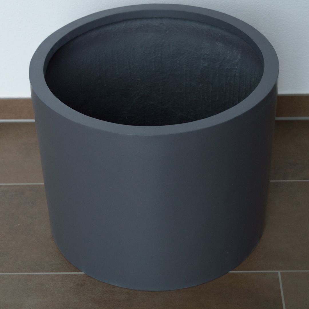 Leerer zylindrischer Pflanzkübel aus Fiberglas in Anthrazit-Metallic auf braunen Fliesen vor einer weißen Wand