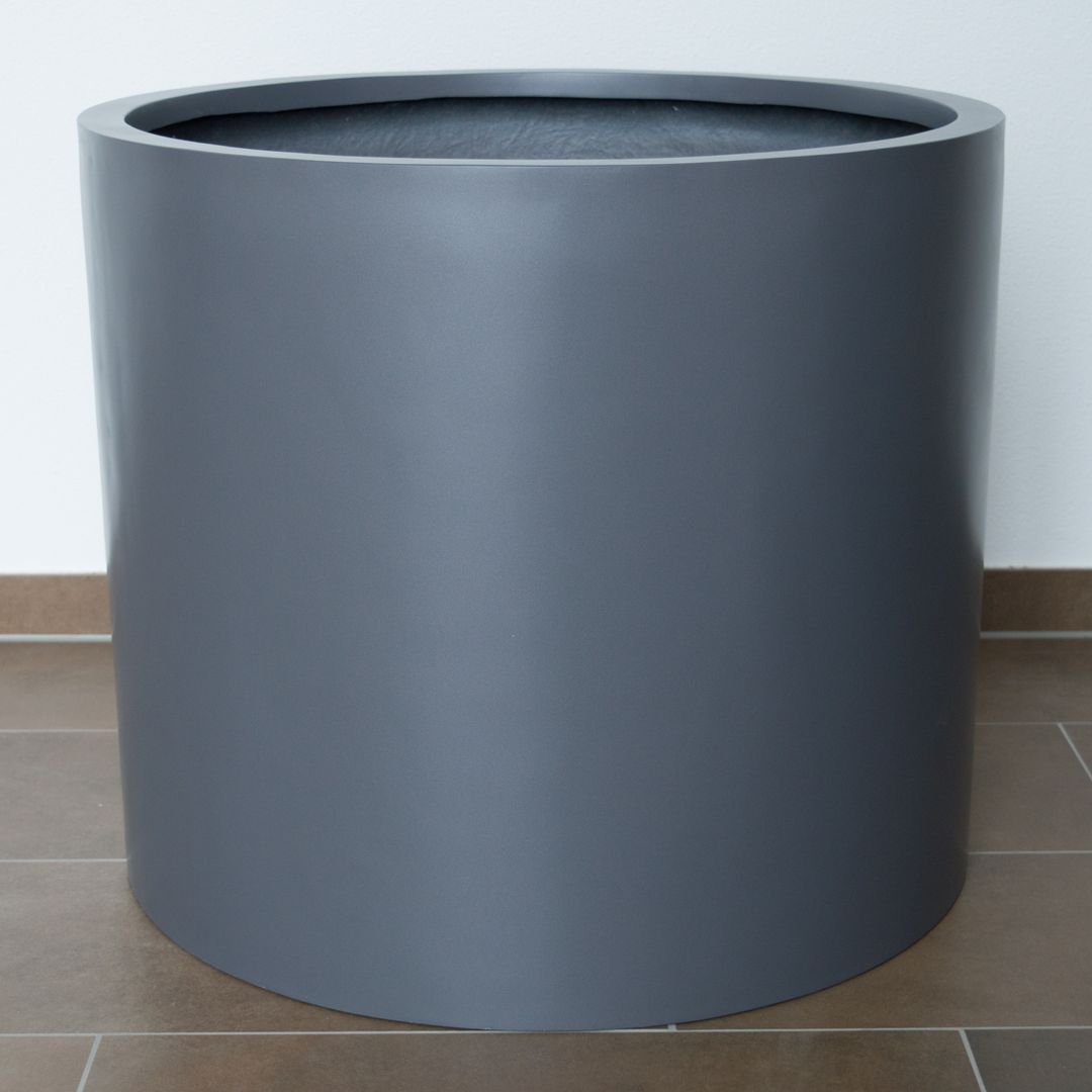 Zylindrischer Pflanzkübel aus Fiberglas in Anthrazit-Metallic vor weißer Wand auf braunem Fliesenboden