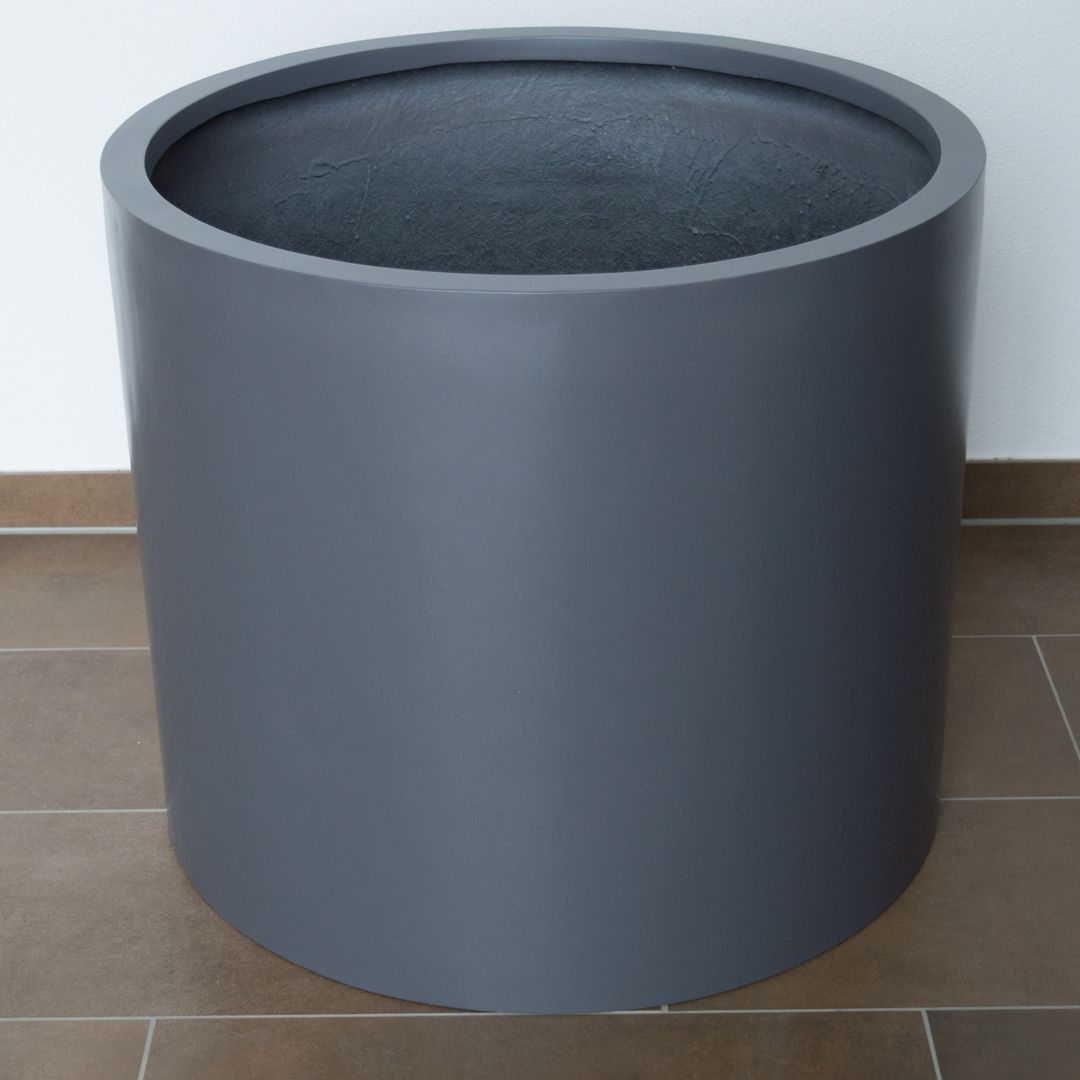 Leerer zylindrischer Pflanzkübel aus Fiberglas in Anthrazit-Metallic auf braunem Fliesenboden vor weißer Wand