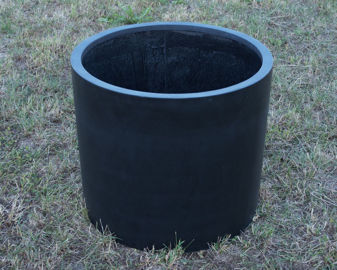 Schwarz-matter zylindrischer Pflanzkübel aus Fiberglas, leer auf einer Rasenfläche, Blick von schräg oben