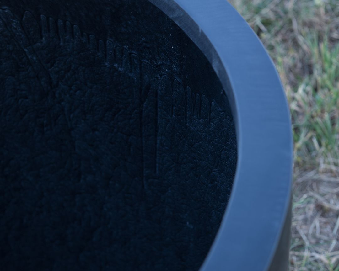Nahaufnahme des runden Rands eines schwarz-matten Pflanzkübels aus Fiberglas mit Blick ins Innere, auf Rasen stehend