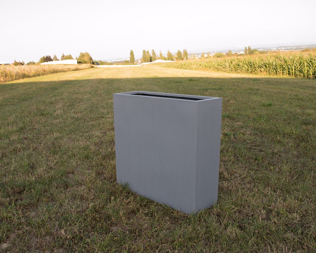 Grauer rechteckiger Pflanzkübel aus Fiberglas als Raumteiler, unbepflanzt auf einer Wiese im Freien
