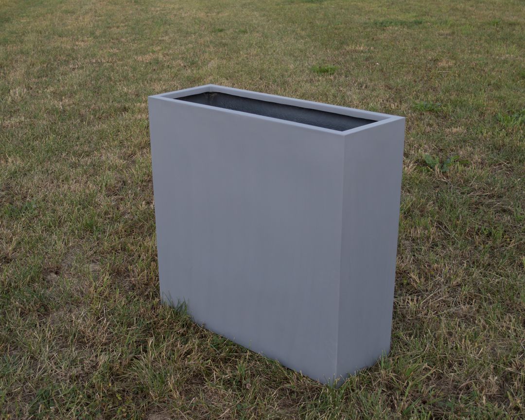 Grauer rechteckiger Pflanzkübel aus Fiberglas in schmaler Raumteiler-Form, leer auf einer Rasenfläche im Freien