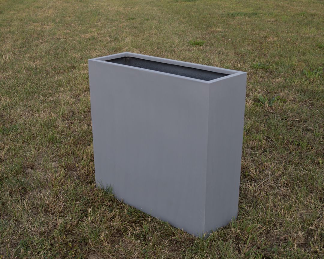 Grauer rechteckiger Pflanzkübel aus Fiberglas in schmaler Raumteiler-Form, leer auf einer Rasenfläche im Freien