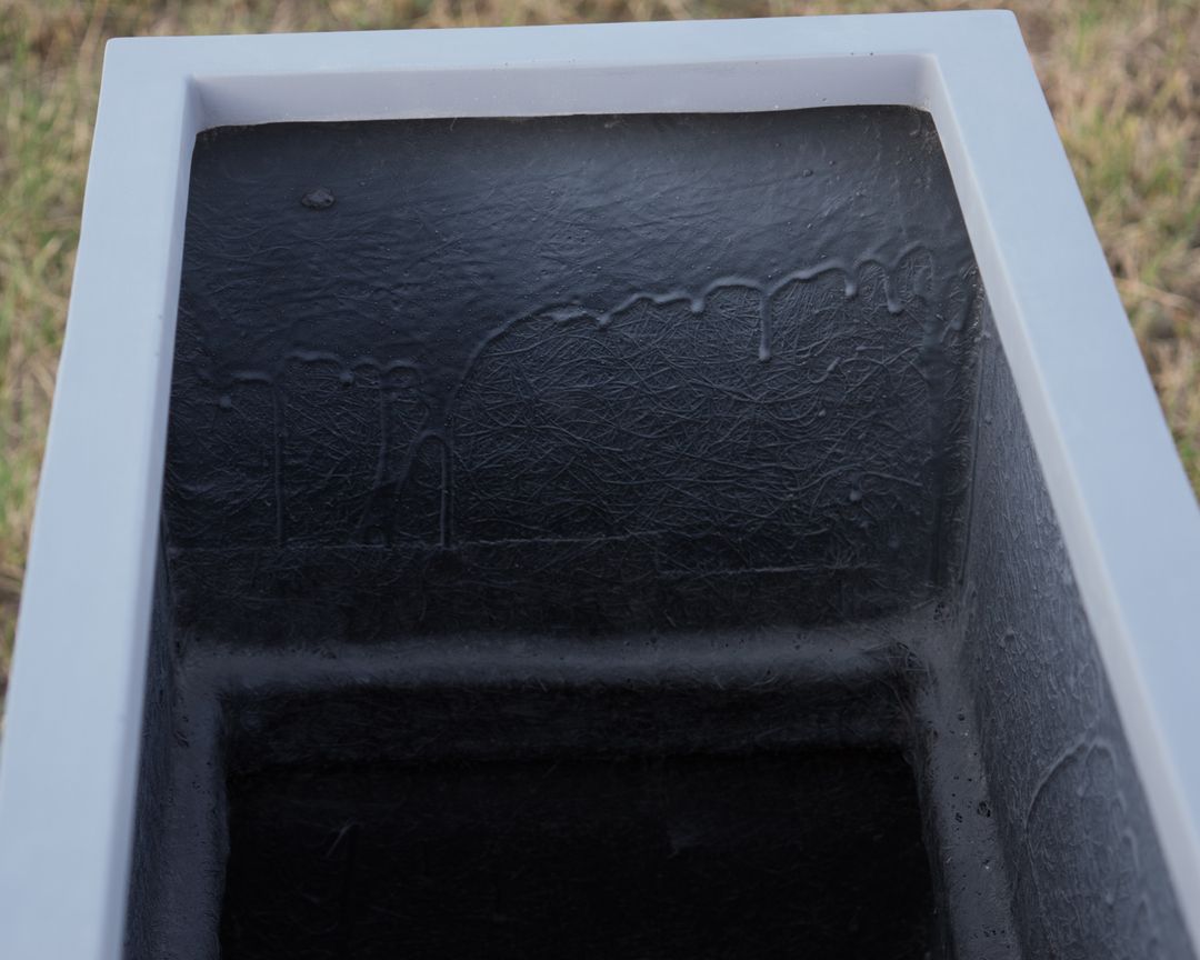Blick von oben in einen grauen rechteckigen Pflanzkübel aus Fiberglas mit dunkler, faseriger Innenwand
