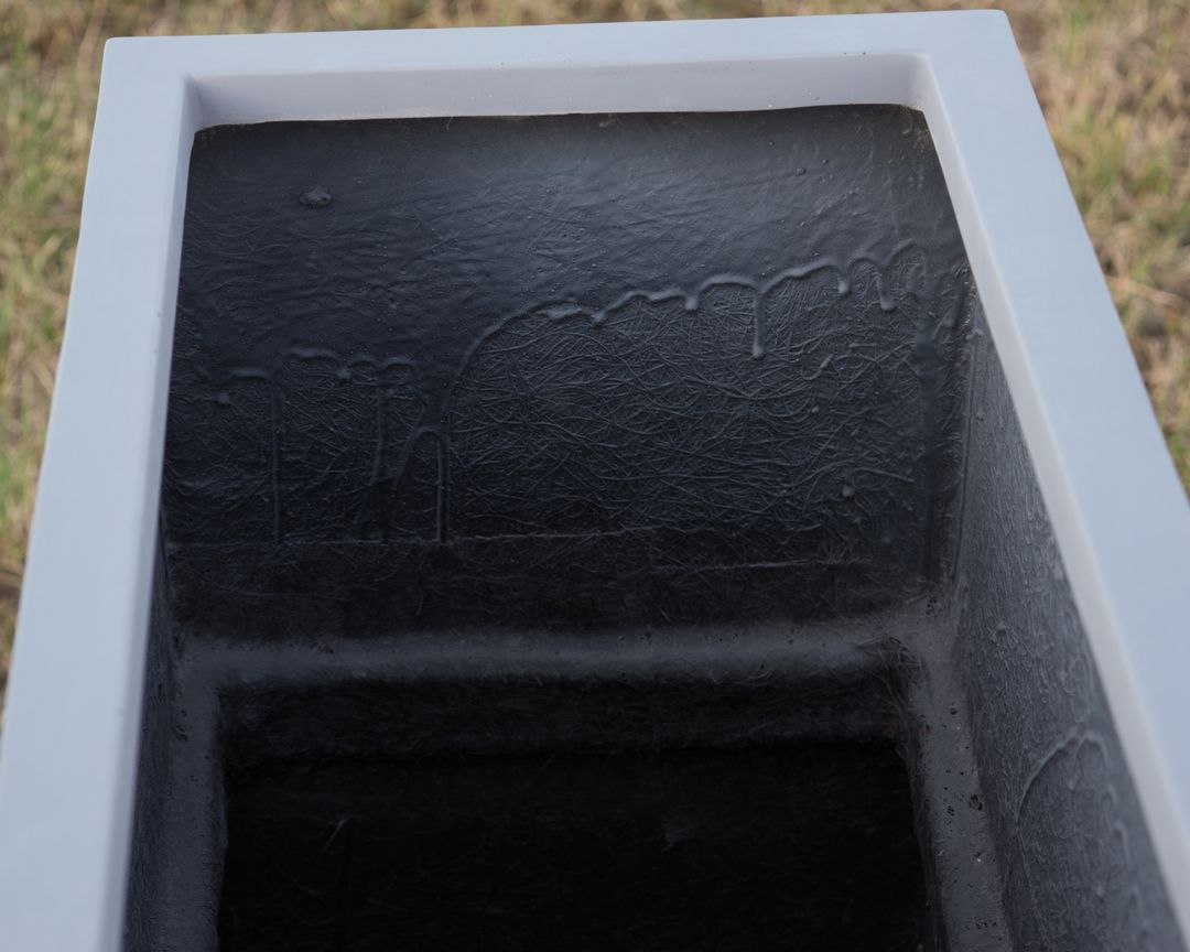 Blick von oben in einen grauen rechteckigen Pflanzkübel aus Fiberglas mit dunkler, faseriger Innenwand