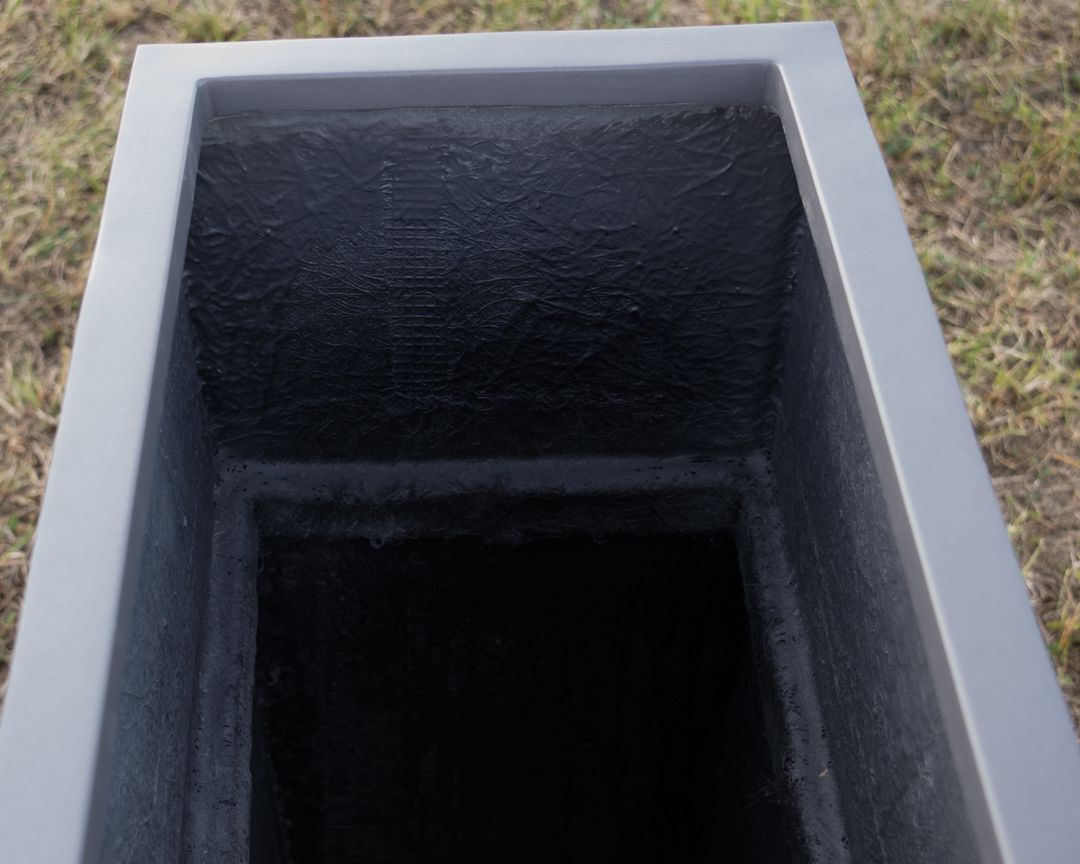Blick von oben in einen schmalen rechteckigen Pflanzkübel in Anthrazit-Metallic mit dunkler, rauer Innenseite auf Rasen