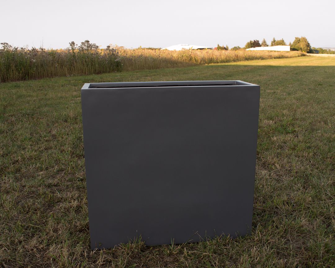 Rechteckiger Pflanzkübel aus Fiberglas in Anthrazit metallic ohne Bepflanzung auf einer Wiese vor einem Feld