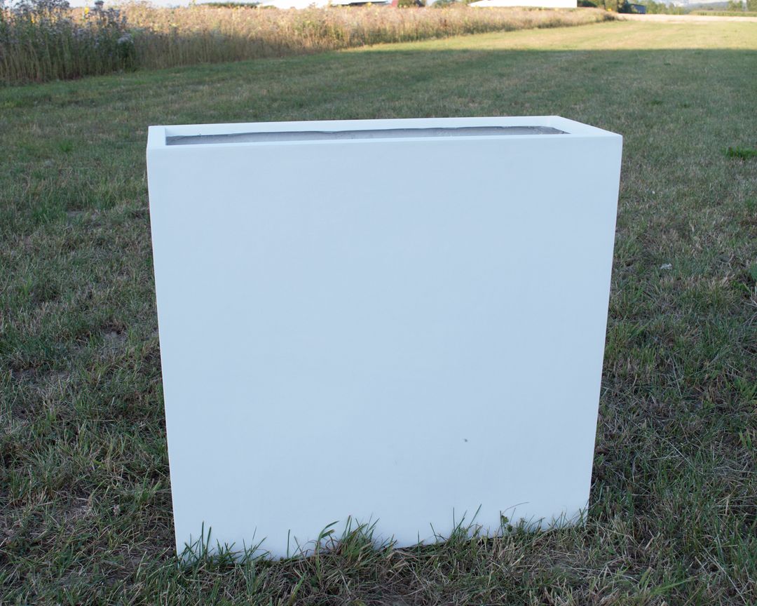 Rechteckiger Pflanzkübel aus Fiberglas in Perlmuttweiß, leer auf einer Rasenfläche vor einem Feld