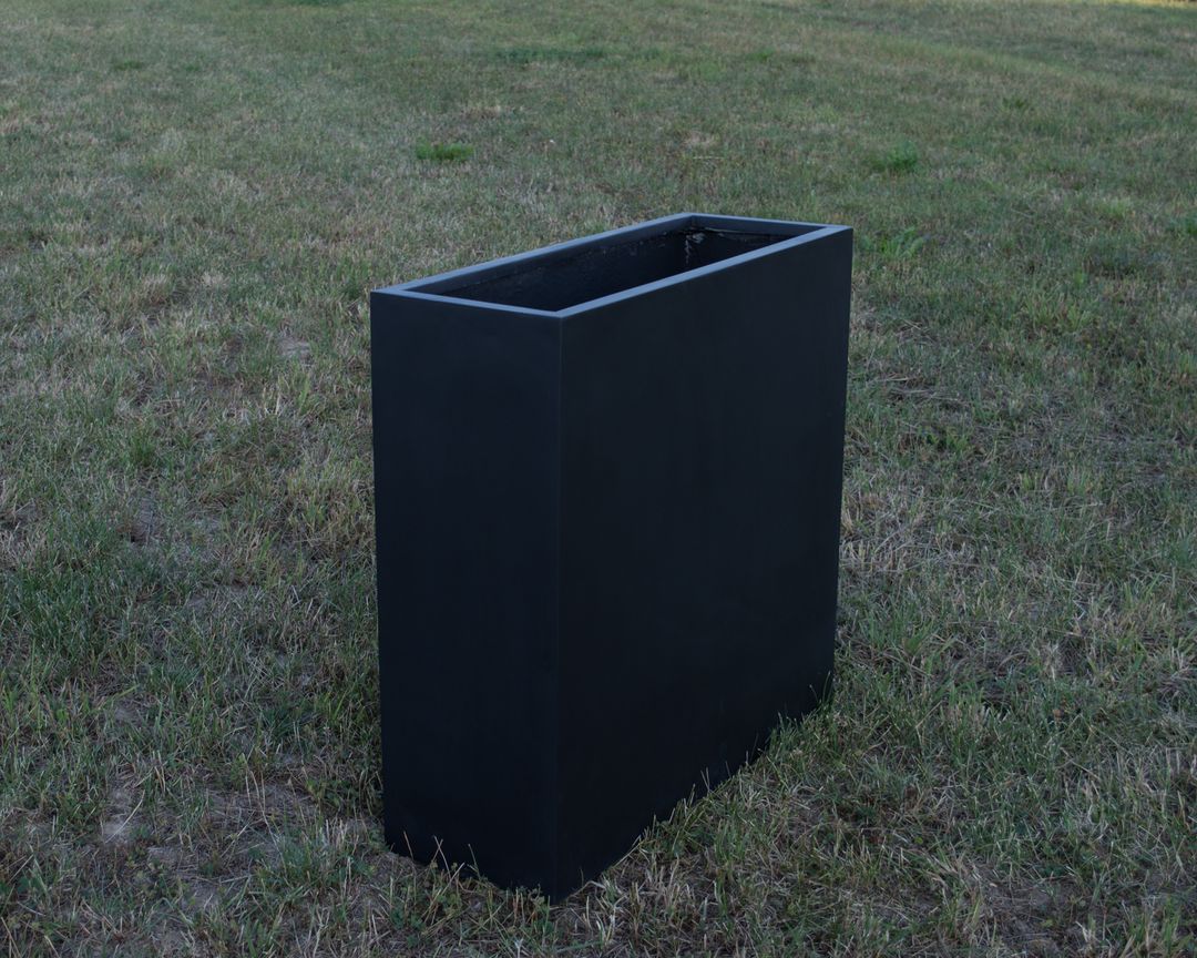 Rechteckiger Pflanzkübel aus Fiberglas in Schwarz-matt, hoch und schmal, leer auf einer Rasenfläche im Freien