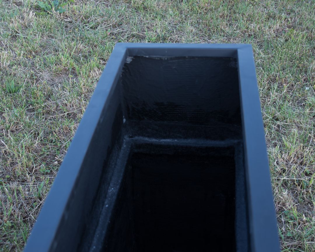 Blick von oben in einen schwarz-matten rechteckigen Pflanzkübel aus Fiberglas mit sichtbarem Innenraum auf Rasen