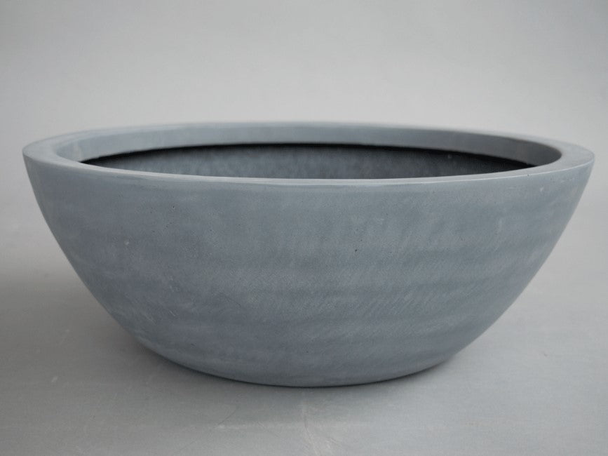 Runde, flache Pflanzschale aus Fiberglas in Grau mit leicht gewischter Oberfläche vor grauem Hintergrund