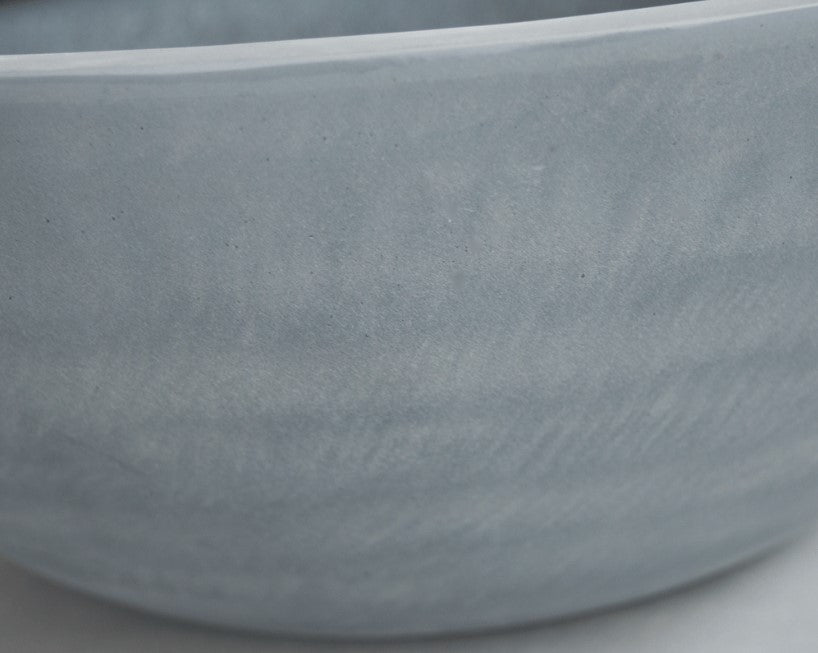 Nahaufnahme der gewölbten Außenwand einer runden Pflanzschale aus Fiberglas in Grau mit matter, leicht gewolkter Oberfläche