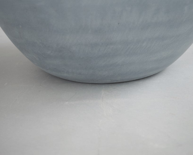 Nahaufnahme der gerundeten Unterseite einer grauen Pflanzschale aus Fiberglas mit sichtbarer Oberflächenstruktur