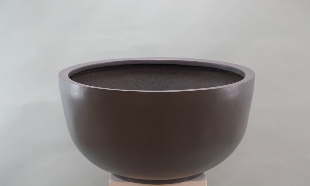 Runde Pflanzschale aus Fiberglas in Anthrazit-Metallic auf einem hellen Sockel vor grauem Hintergrund