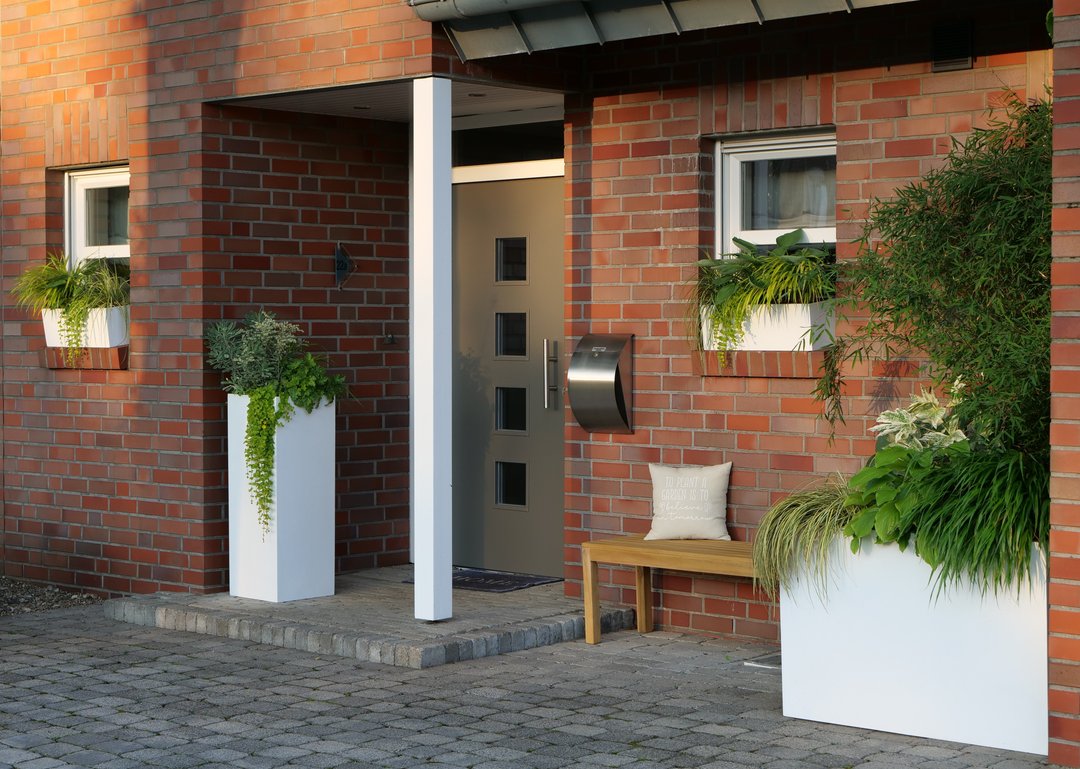 Pflanzkübel Fiberglas Säule 38x38x100cm perlmutt weiß mit hängender Bepflanzung neben der Haustür eines Klinkerhauses