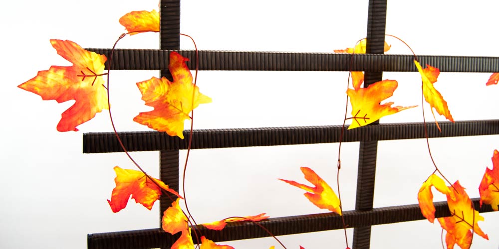 Rankgitter aus Polyrattan in Mocca als Detail, mit einer Girlande aus orange-gelben Herbstblättern dekoriert