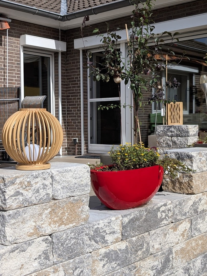 Pflanzkübel Fiberglas oval 65x31xH25cm hochglanz rot mit gelben Blüten auf der Natursteinmauer einer Terrasse
