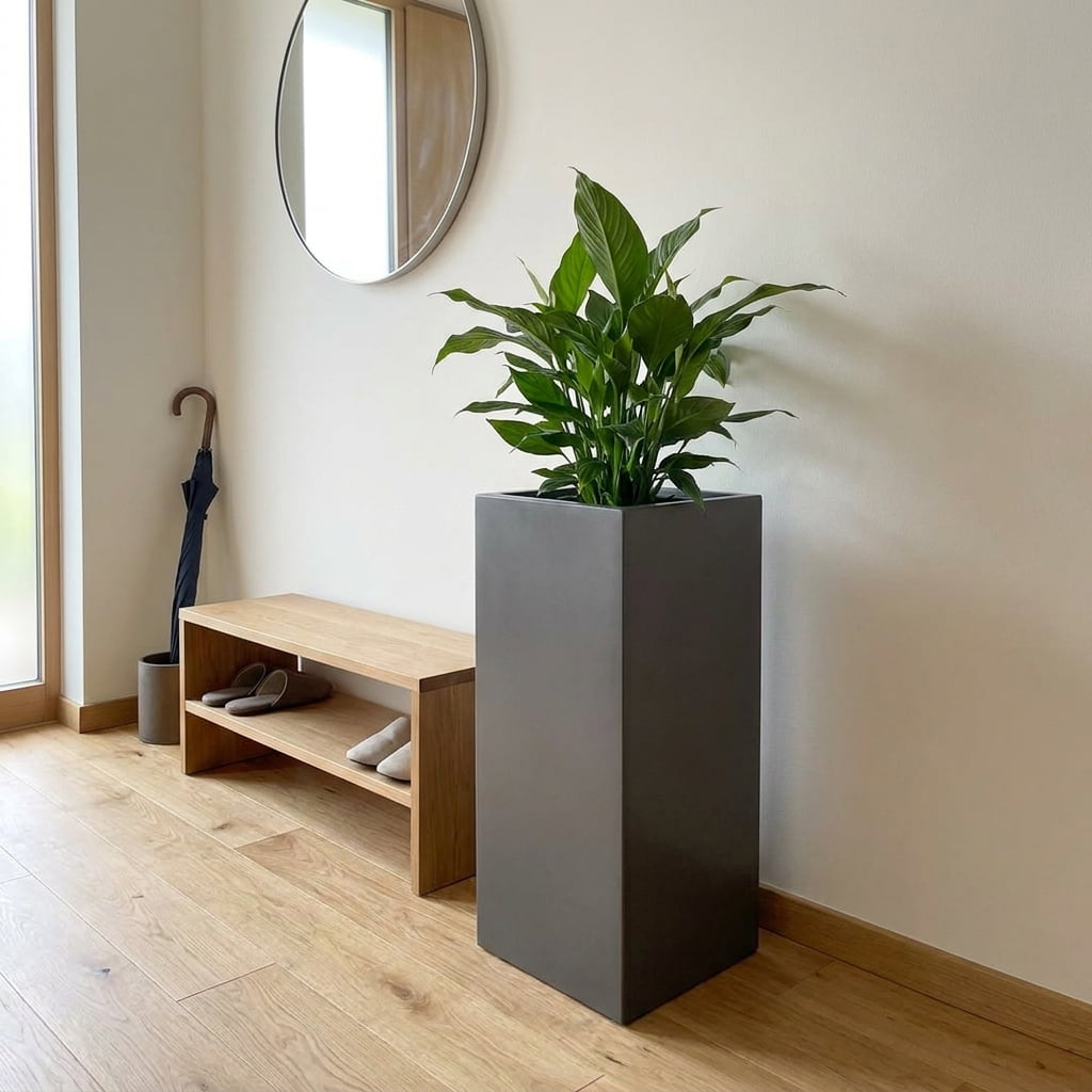 Anthrazit metallic Pflanzkübel in Säulenform mit Einblatt neben einer Holzbank mit Hausschuhen im hellen Flur