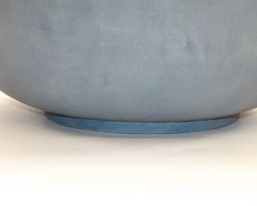 Nahaufnahme vom Boden einer runden grauen Pflanzschale aus Fiberglas mit flachem Standring auf hellem Untergrund