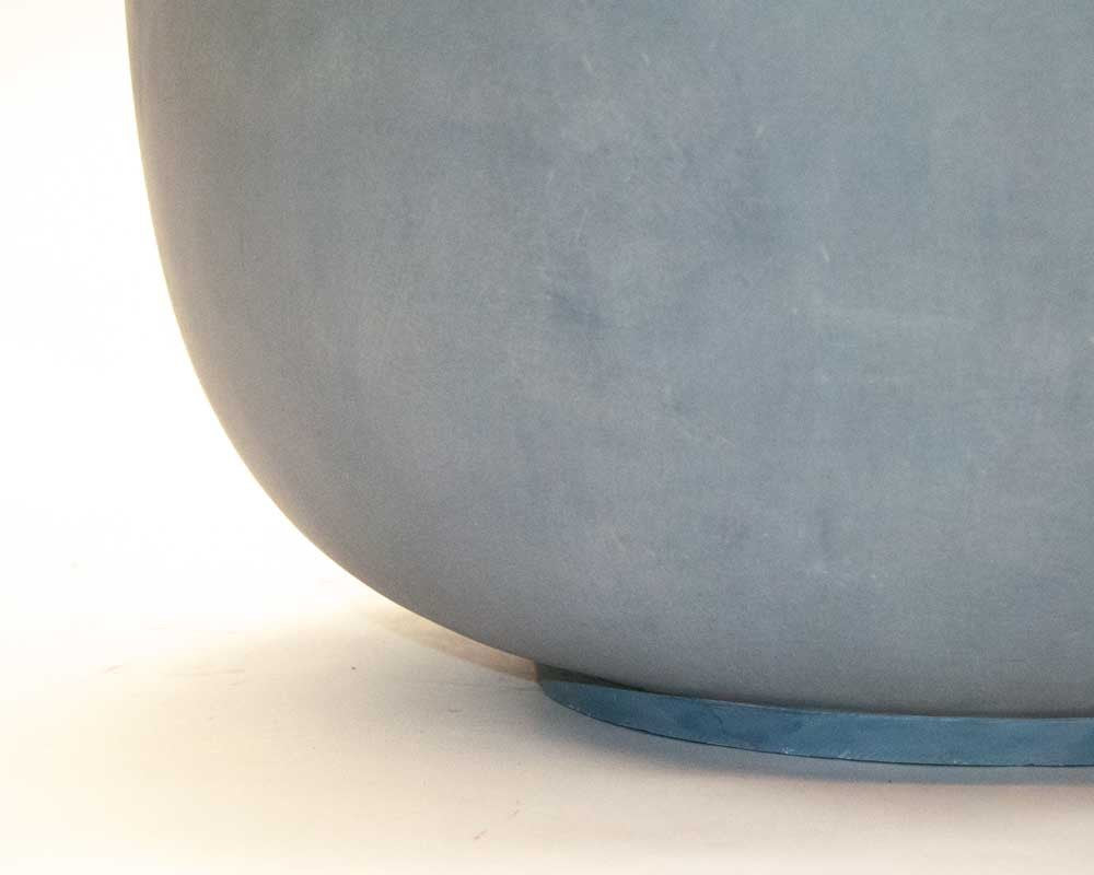 Nahaufnahme der abgerundeten Unterkante einer grauen runden Pflanzschale aus Fiberglas mit flachem Standring